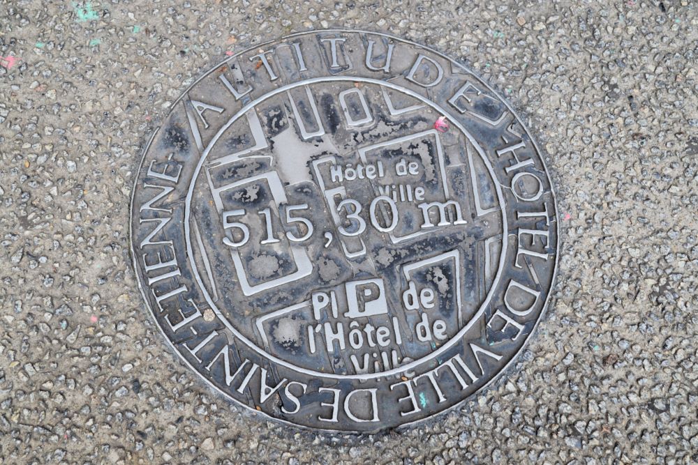 une plaque d'égout de Saint Etienne avec indiquée dessus la localisation à côté de l'hôtel de ville et l'altitude 515,30 mètres
