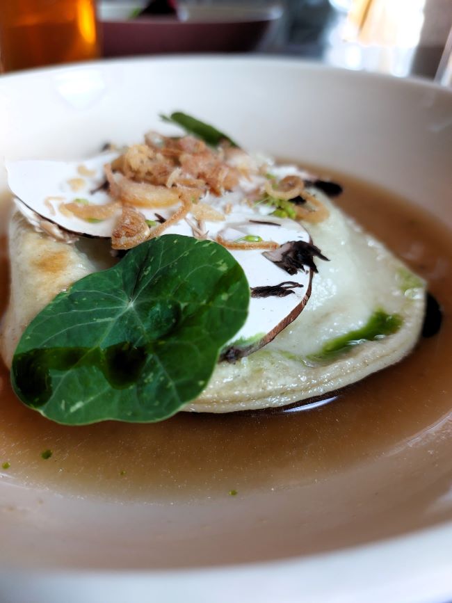 raviole servie dans un bouillon et surmontée d'une feuille de capucine