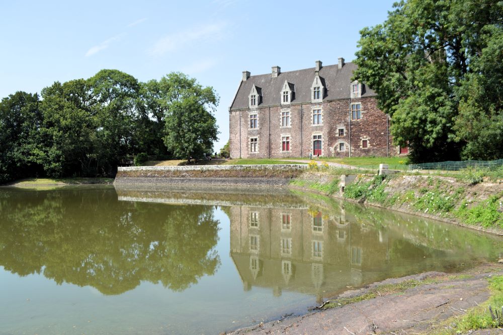 un château de la Renaissance en schiste rouge se reflète dans un étang bordé d'arbres
