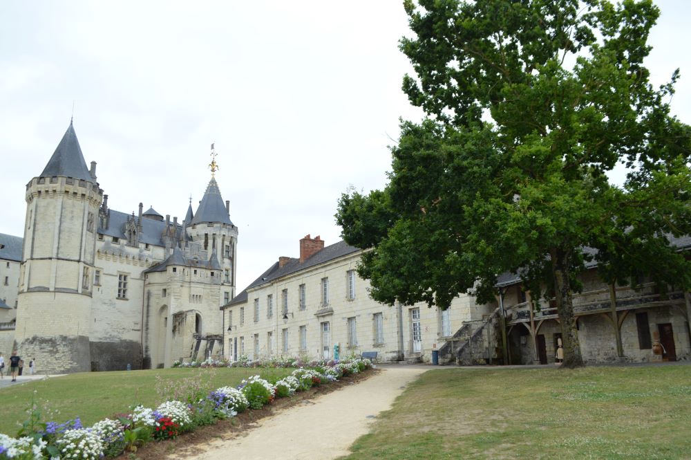des batiments anciens en pierre blanche dans un parc avec le château au fond