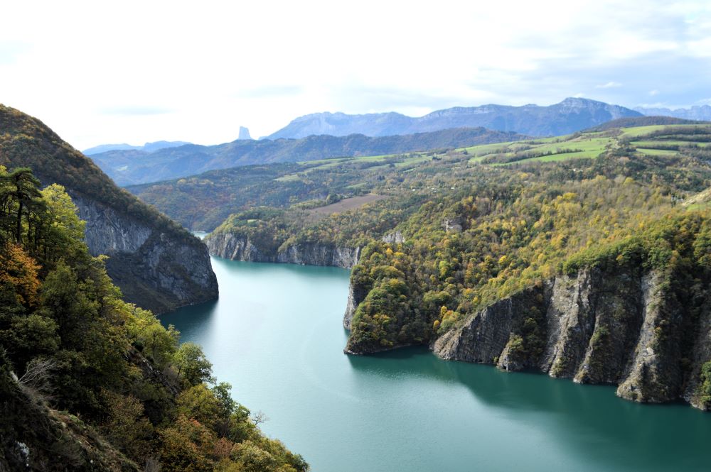 un lac dans un canyon bordé d'arbres aux couleurs de l'automne avec des silhouettes de montagne au fond