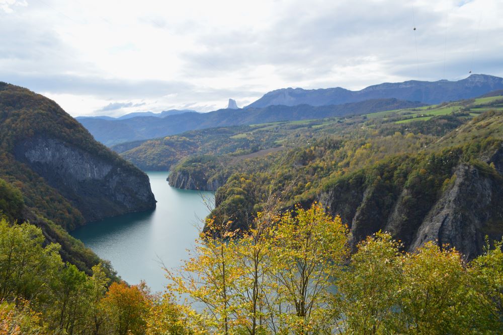 un lac dans un canyon bordé d'arbres aux couleurs de l'automne avec des silhouettes de montagne au fond
