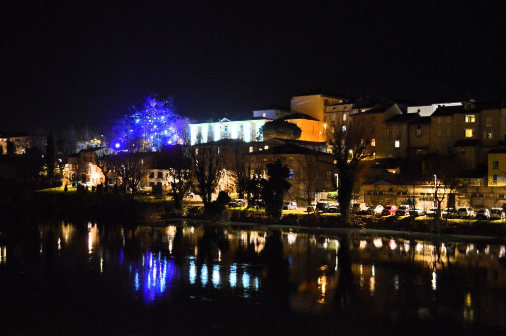 une ville de nuit, éclairée en couleurs et qui se reflète dans une rivière