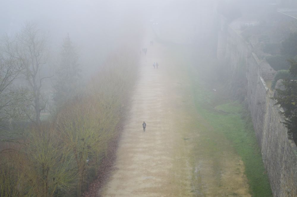 des personnes se promènent au pied d'un rempart dans le brouillard
