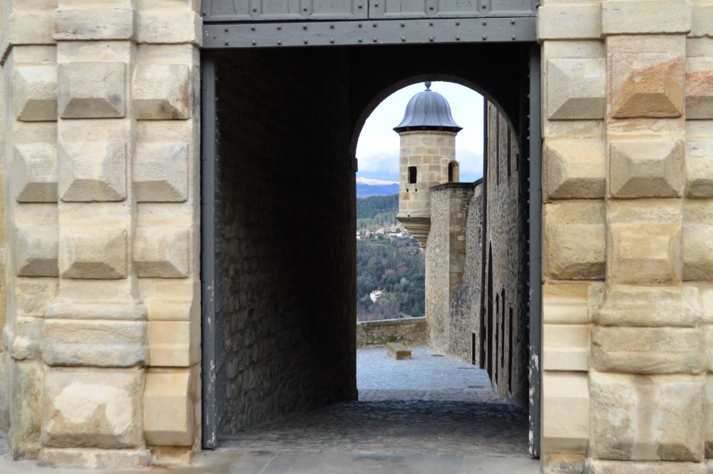 une porte qui donne accès à une rue pavée longeant le château