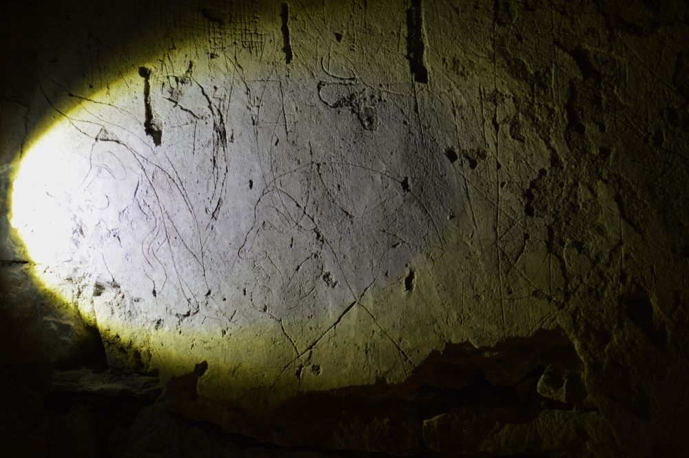 des graffitis du 18e siècle dans le sous sol d'un château, éclairés à la lampe torche