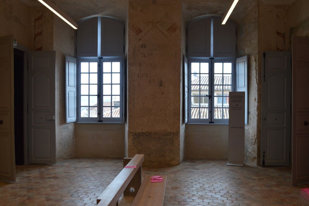 une salle au sol en tomettes avec deux grandes fenêtres