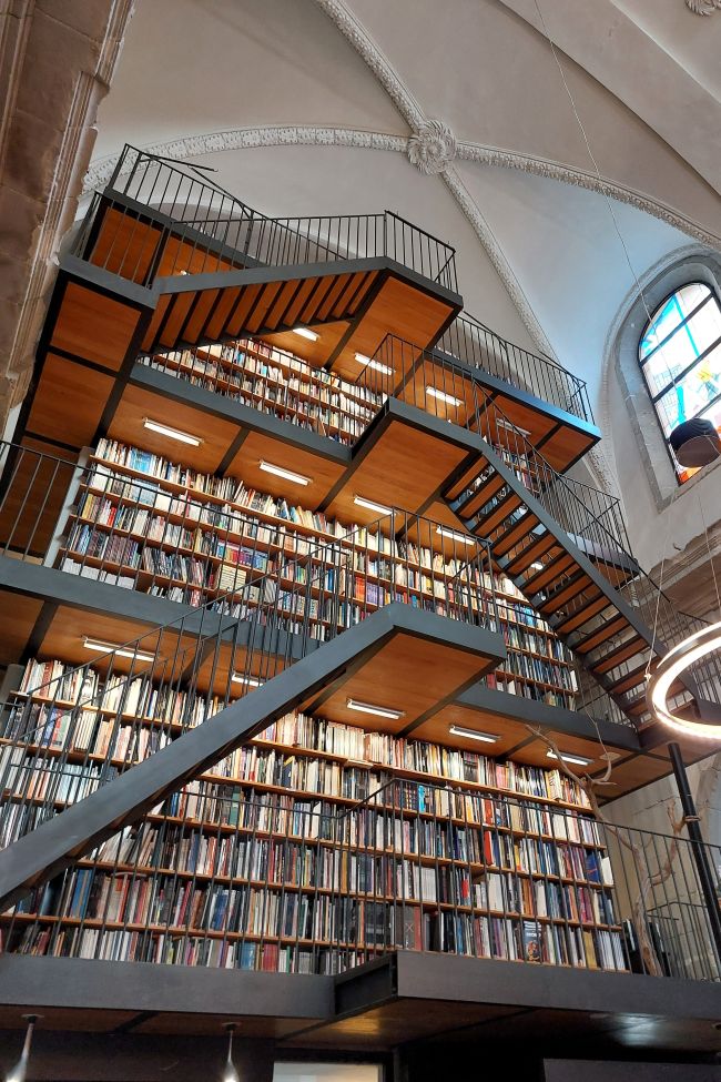 un mur de livres sur plusieurs étages auquel on accède par des escaliers modernes en bois