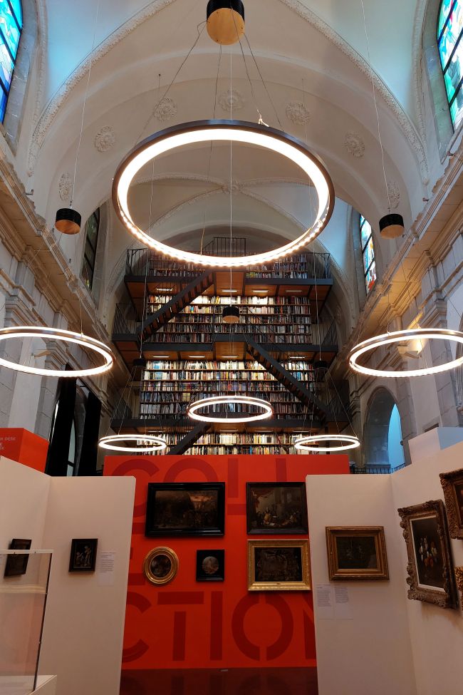 une galerie d'art dans une ancienne chapelle, avec un mur de livres au fond