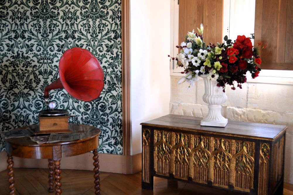 un gramophone dont le pavillon est rouge est posé sur une table et fait face à un bouquet rouge et blanc sur un coffre
