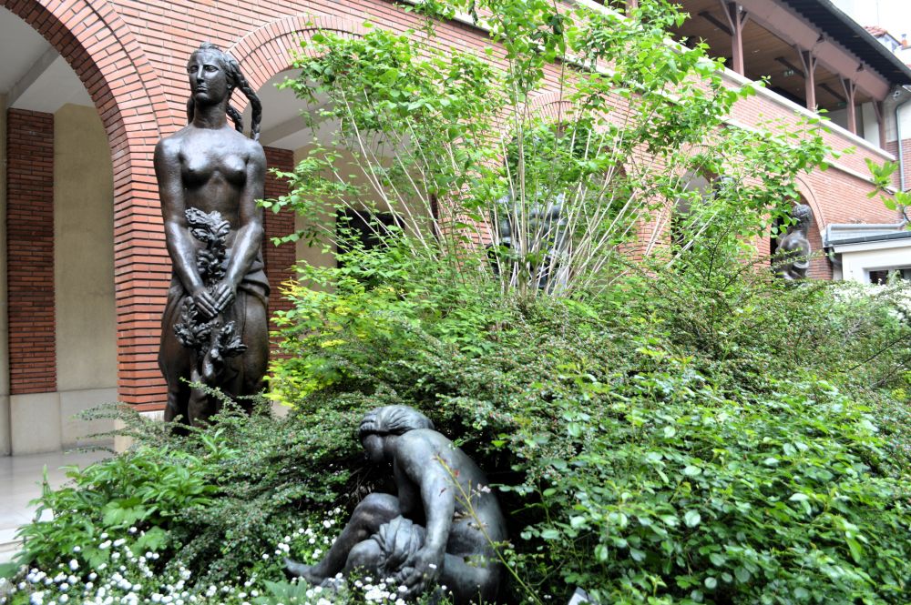 deux sculptures en bronze dans un jardin devant un bâtiment en briques