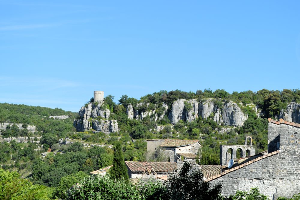au premier plan un village ancien, au second plan des falaises calcaires avec une tour de guêt