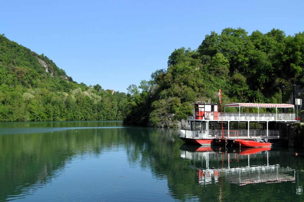 sur une rivière entourée de rives boisées, un bateau de type bateau à roue à aube est amarré à quai