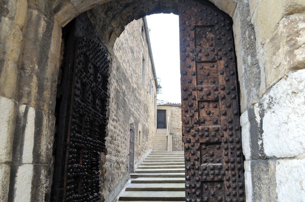 une porte massive en bois clouté ouverte sur un escalier qui monte