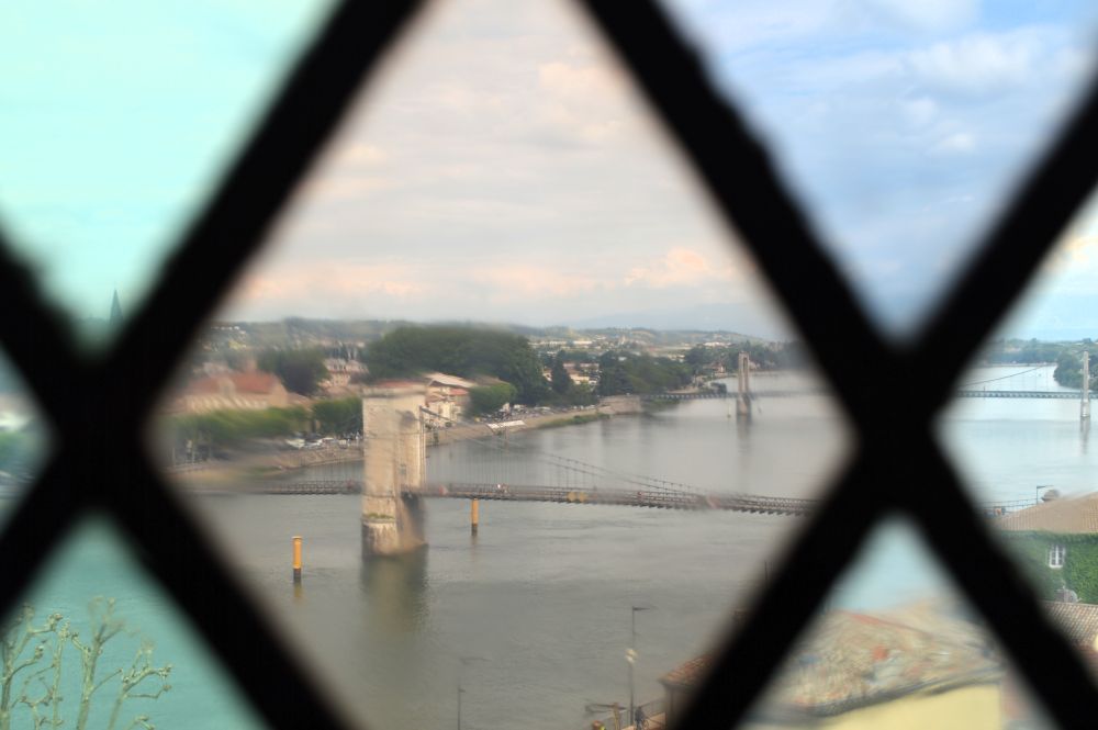 à travers une fenêtre aux carreaux en losange et colorés, vue sur le Rhône et la passerelle suspendue Marc Seguin depuis le château de Tournon