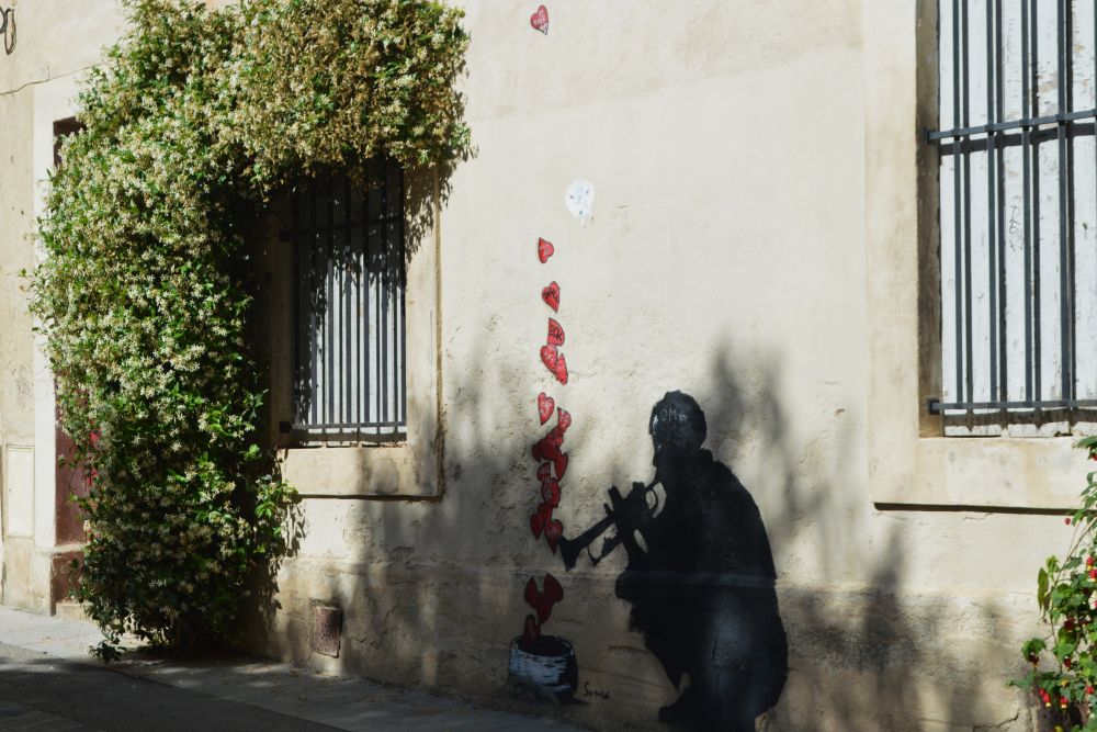 un collage street art représentant un musicien avec des coeurs qui s'envolent de sa trompette sur une façade fleurie d'un jasmin