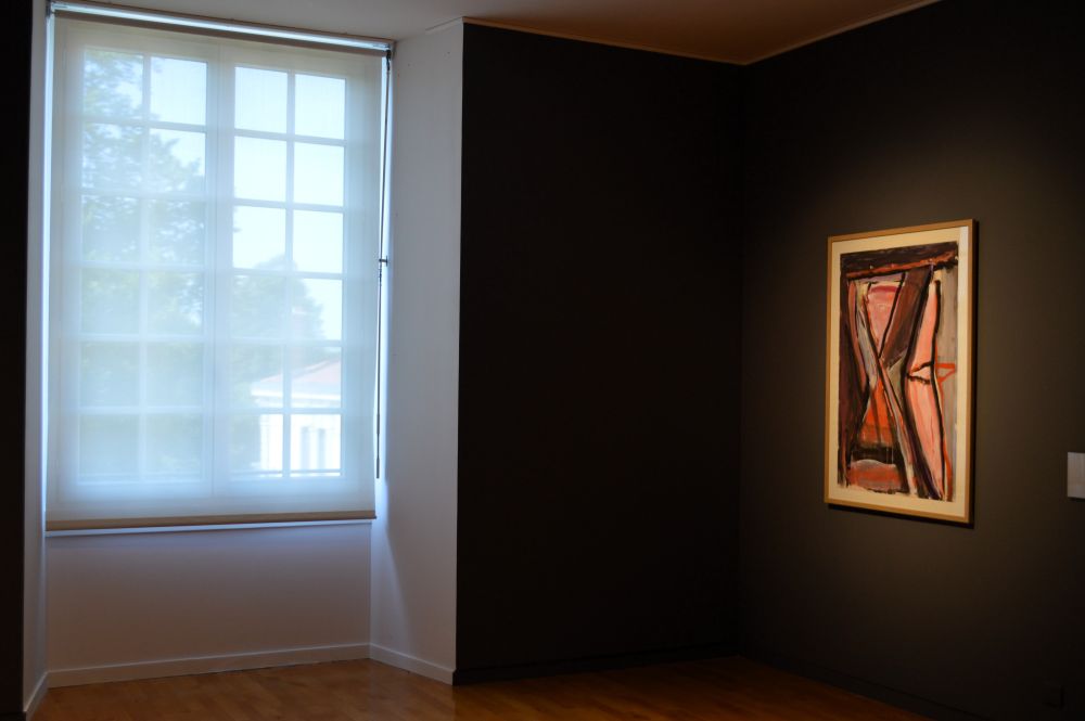 une fenêtre éclaire une pièce aux murs noirs avec un tableau de Bram van Velde