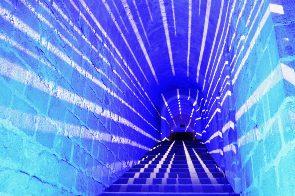 parcours nocturne de l'abbaye du Mont Saint Michel avec des rayons de lumière dans un escalier