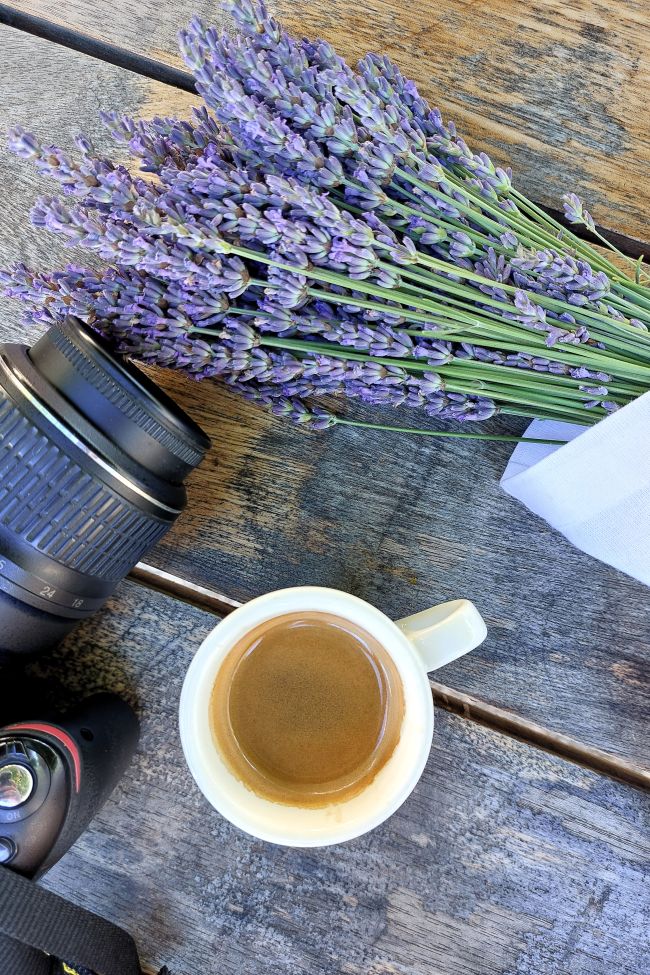 un café, un appareil photo et un bouquet de lavande sur une table en bois