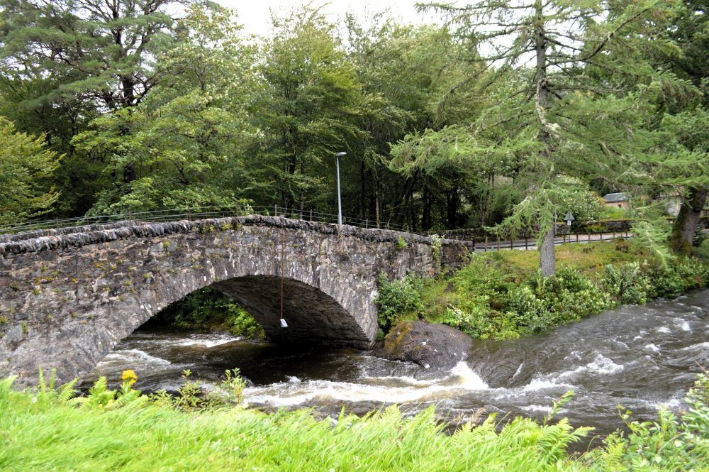 un petit pont de pierre au dessus d'une rivière en crue