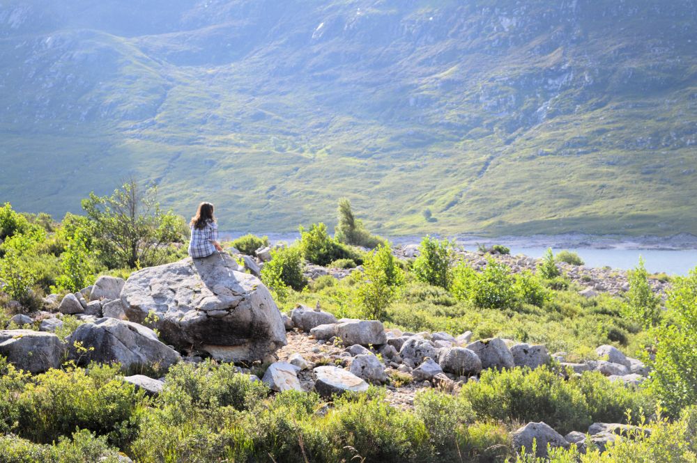 une personne assise au sommet d'un rocher avec vue sur un lac de montagne