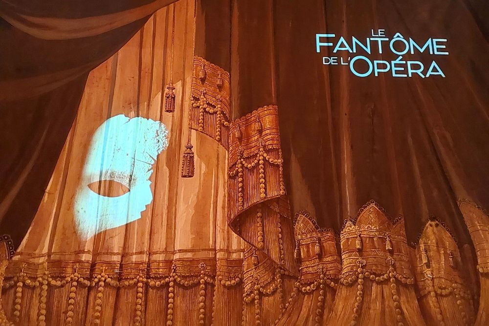 Rideau de scène du théâtre Antoine à Paris avec une projection lumineuse indiquant le Fantôme de l'Opéra
