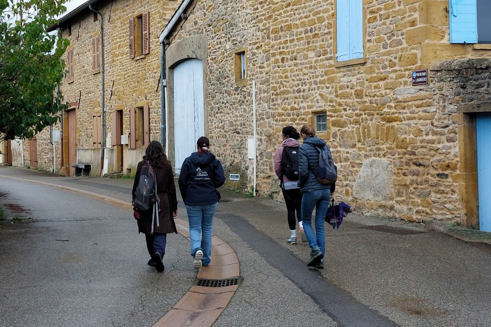 un groupe de 4 personnes de dos dans une rue de village bordée de maisons en pierres dorées