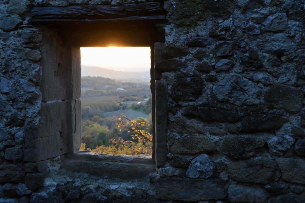 vue sur un paysage au coucher de soleil à travers une ouverture dans un mur en pierres