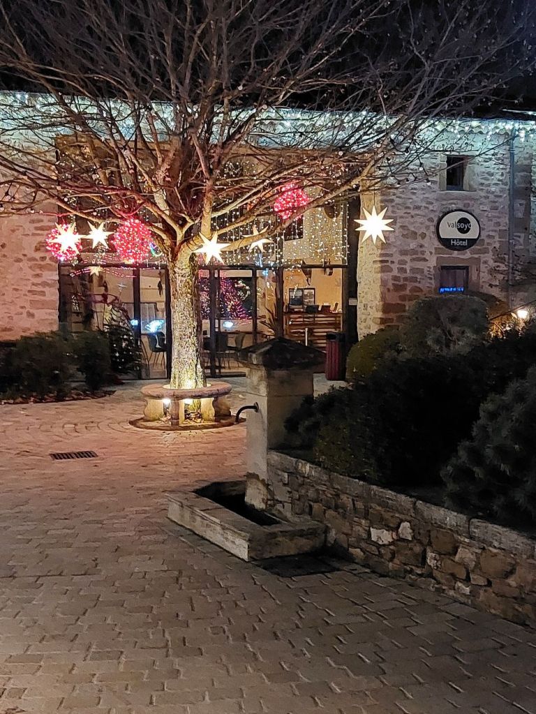 une cour devant un batiment en pierre avec un arbre décoré de boules et d'étoiles lumineuses