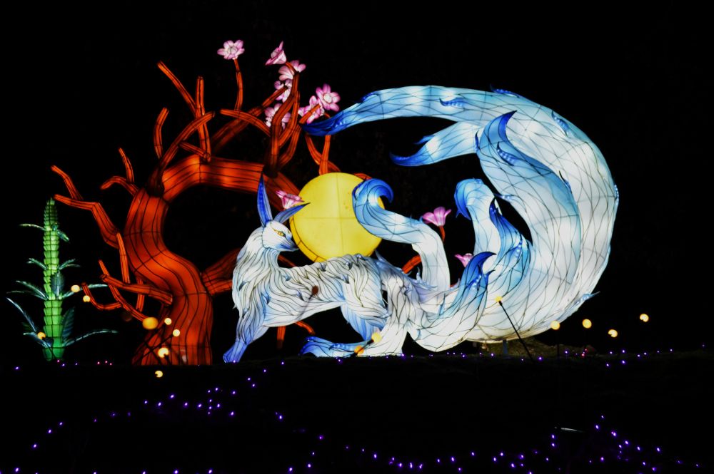 Sculptures lumineuses en forme de kitsune au pied d'un cerisier en fleurs