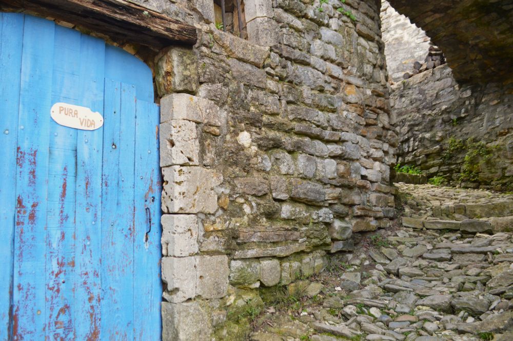 une porte bleue avec l'inscription "pura vida" dans une calade bordée de bâtiments en pierres