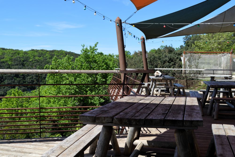 une terrasse en bois, ombragée par des voilages, face à la forêt