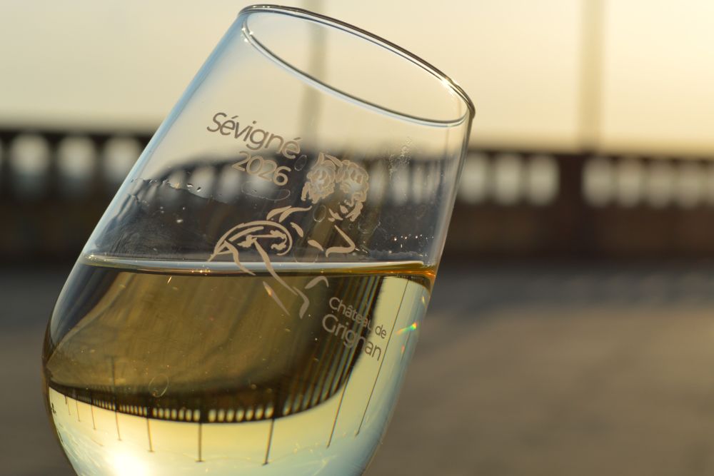 reflet de la balustrade du château de Grignan dans un verre de vin blanc avec un logo Sévigné 2026