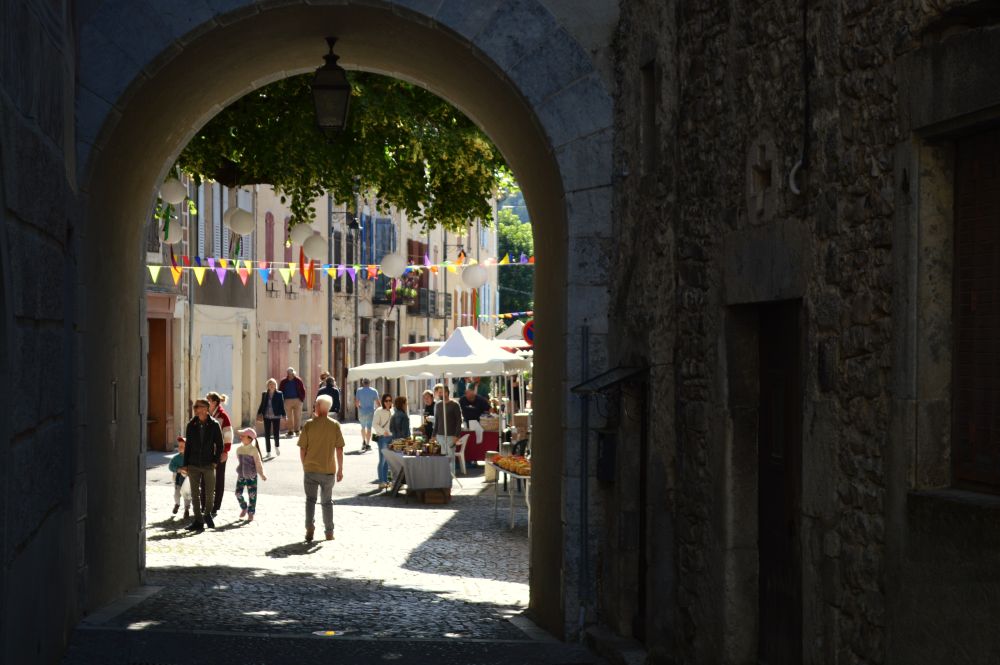 vue sur un marché dé village à travers une porte médiévale