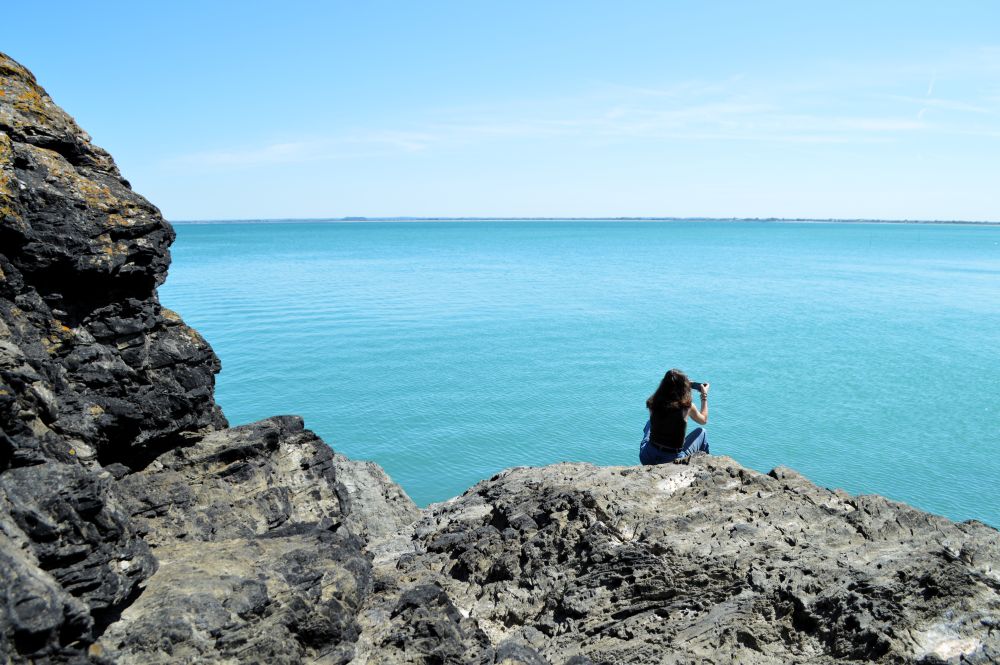 personne assise sur des rochers face à la mer